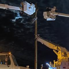夜间，两辆铲斗卡车上的电线工人在电线杆上工作.  